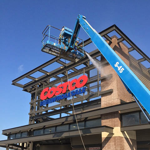 A crane is lifting a sign onto a building.
